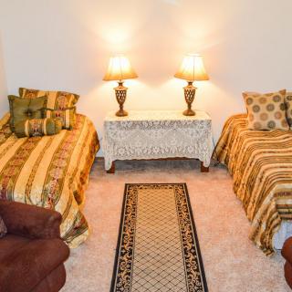 A cozy bedroom featuring twin beds with decorative pillows, a central side table with two lamps, and a patterned carpet on the floor.