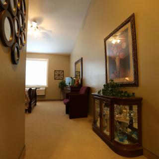 A warmly lit hallway featuring decorative mirrors, a ceiling fan, and elegant furniture with a glass display cabinet.