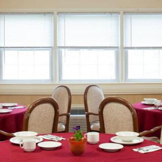 A neatly arranged dining room with red tablecloths and place settings on each table.