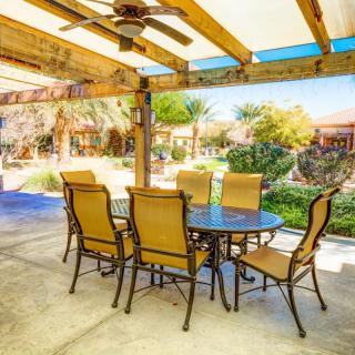 Outdoor patio area with a table and chairs under a pergola, overlooking a lush garden.
