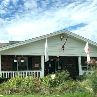 A charming building with a welcoming porch, adorned with flags and surrounded by greenery.