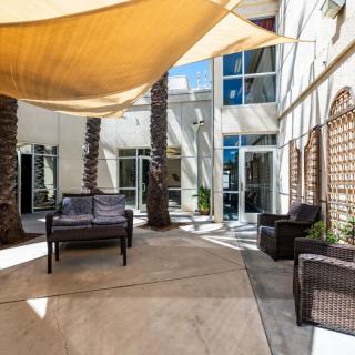 A sunny outdoor patio with shade sails, wicker furniture, and palm trees.