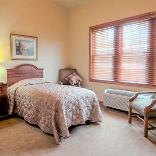 A cozy bedroom with a single bed, lamp, and window with blinds.