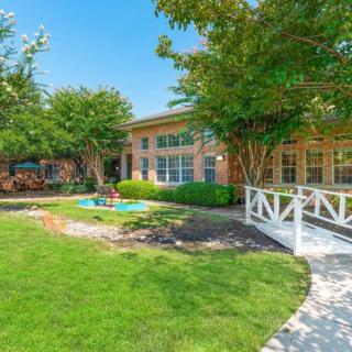 A scenic view of a building surrounded by a lush garden with trees and a well-maintained lawn.