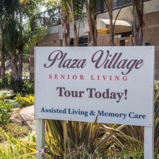 A sign for Plaza Village Senior Living, promoting tours and offering assisted living and memory care services.