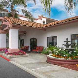 The image shows the entrance of a hotel with landscaped gardens and outdoor seating.