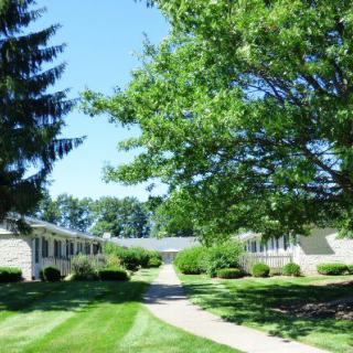 A serene apartment complex with well-maintained landscaping, featuring lush green grass and large trees on a sunny day.
