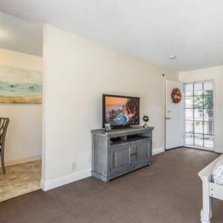 A cozy living room with a television and modern furniture, featuring a view of the adjacent dining area.