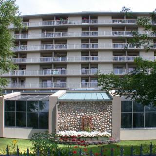 A multi-story hotel building with several balconies, surrounded by trees.