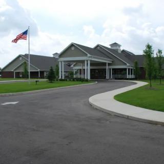 A large building with a driveway, an American flag, and a grassy lawn in front.