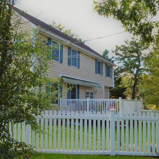 A suburban house with a white fence and surrounding trees.