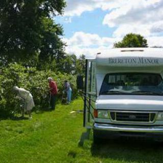 People gardening near a parked bus in a lush outdoor setting.