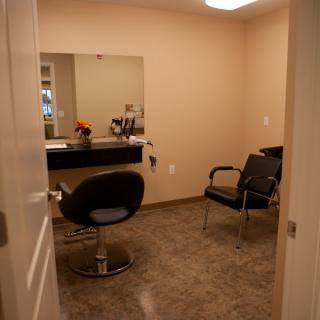 A salon room featuring a styling chair and mirror with a small waiting area.