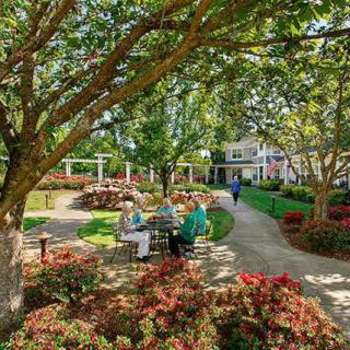 A serene garden scene with people sitting and walking among blooming flowers and lush trees.