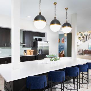 A modern kitchen with pendant lights, dark cabinetry, and a spacious white countertop with blue bar stools.
