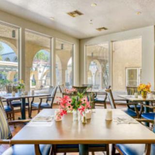 A bright and airy dining area with tables decorated with flowers, surrounded by large windows letting in natural light.