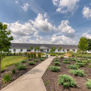 A modern building with a landscaped garden and pathway under a partly cloudy sky.