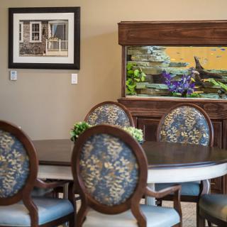 A cozy dining room featuring a round table with floral upholstered chairs, complemented by a large fish tank and wall art.