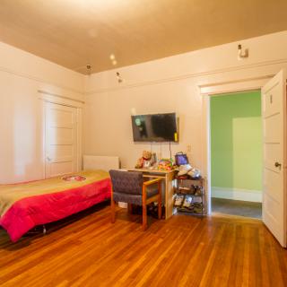 A cozy bedroom featuring a single bed, desk, and television on the wall.