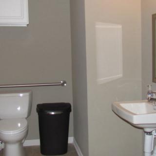 A simple bathroom with a toilet, sink, mirror, and trash can.