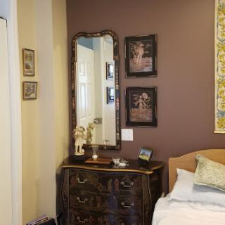 A cozy and elegantly decorated bedroom featuring a vintage mirror and framed artworks.