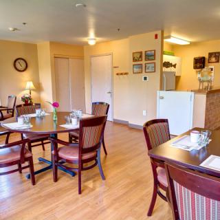 A cozy dining area with neatly arranged tables and chairs, featuring a kitchen space in the background.