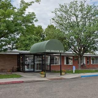 A building entrance with a green awning and surrounding trees.