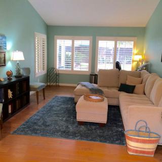 A cozy living room with a beige sofa, blue rug, and large windows providing natural light.