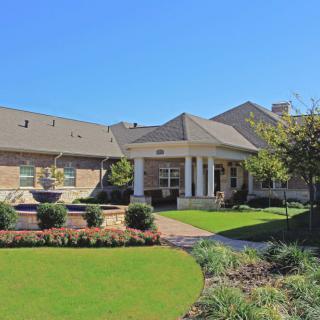 A suburban house with a well-maintained garden and front porch under a clear blue sky.