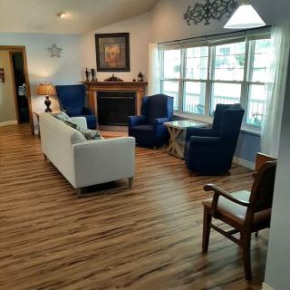 A cozy living room with a white couch, blue armchairs, a fireplace, and large windows.