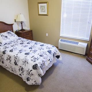 A cozy bedroom with a single bed, a nightstand with a lamp, and a window with blinds.