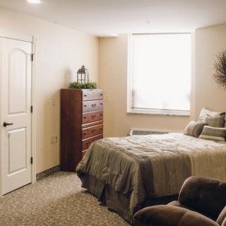 A cozy bedroom with a bed, chest of drawers, and a window allowing natural light.