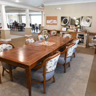 A dining room featuring a long wooden table surrounded by ornate chairs, with artwork adorning the walls.
