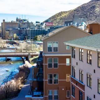 A scenic view of urban buildings along a river, with a bridge and mountains in the background.