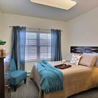A cozy bedroom with a neatly made bed, teal accents, and natural light streaming through the window.