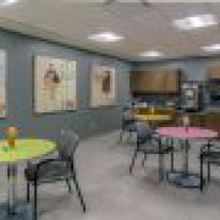 A colorful breakroom with tables, chairs, and artwork on the walls.