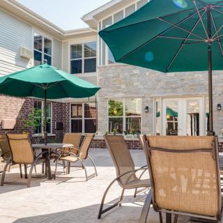An outdoor patio area with tables, chairs, and green umbrellas in front of a building.