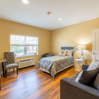 A cozy bedroom with a bed, chair, and lamp on a hardwood floor.
