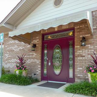 A front entrance with a maroon door, brick facade, and decorative plants.
