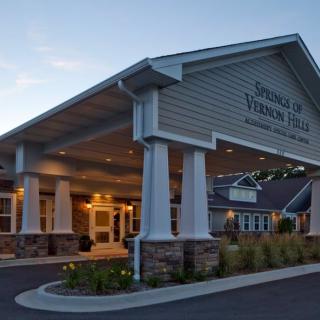 A well-lit building entrance with columns, photographed in the evening.