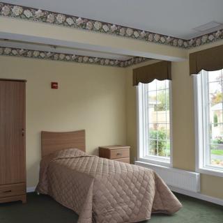 A simple bedroom with a single bed, wardrobe, and large windows.