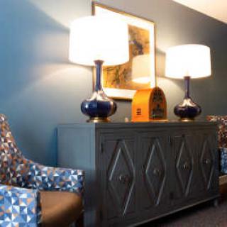 A modern living room setup with a stylish sideboard, two lamps, and patterned chairs against a blue wall.
