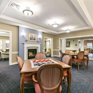 A cozy dining area with tables, chairs, and a fireplace, featuring warm lighting and elegant decor.