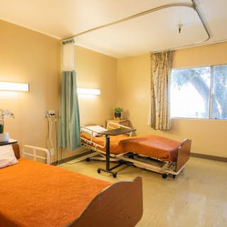 A shared hospital patient room featuring two beds with orange bedding, designed for comfort and care.