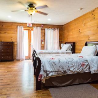 A cozy bedroom with wooden walls featuring two beds, a ceiling fan, and a dresser.