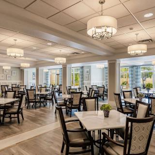 An elegant dining area with neatly arranged tables and chairs, illuminated by chandeliers.
