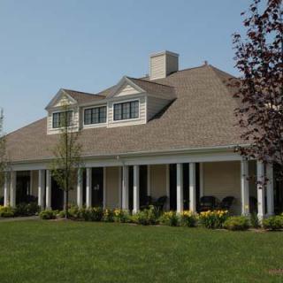 A large house with a sloped roof and columns across the porch, set in a grassy yard.