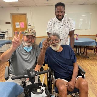 Three friends enjoying a moment together in a care facility, sharing smiles and peace signs.