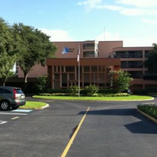 A hospital building with an entrance and a parking lot on a sunny day.