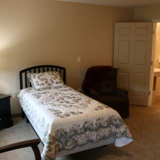 A cozy bedroom featuring a single bed, armchair, and lamp.